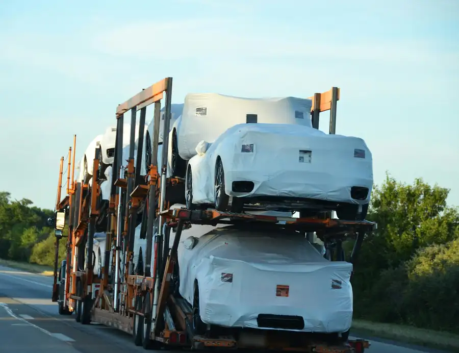 A loaded car carrier with covered new cars heading down a highway